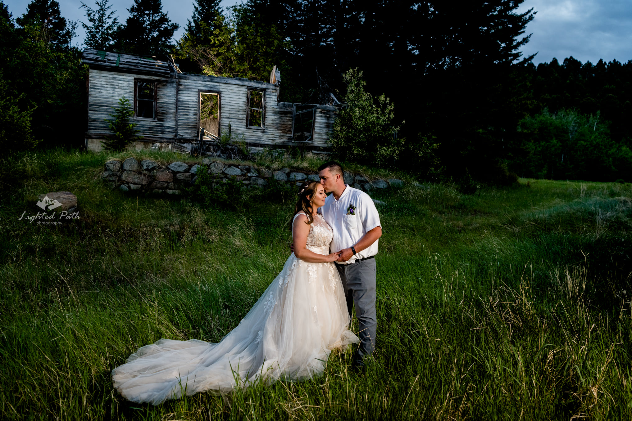 groom kissing bride on the forehead in green grassy field