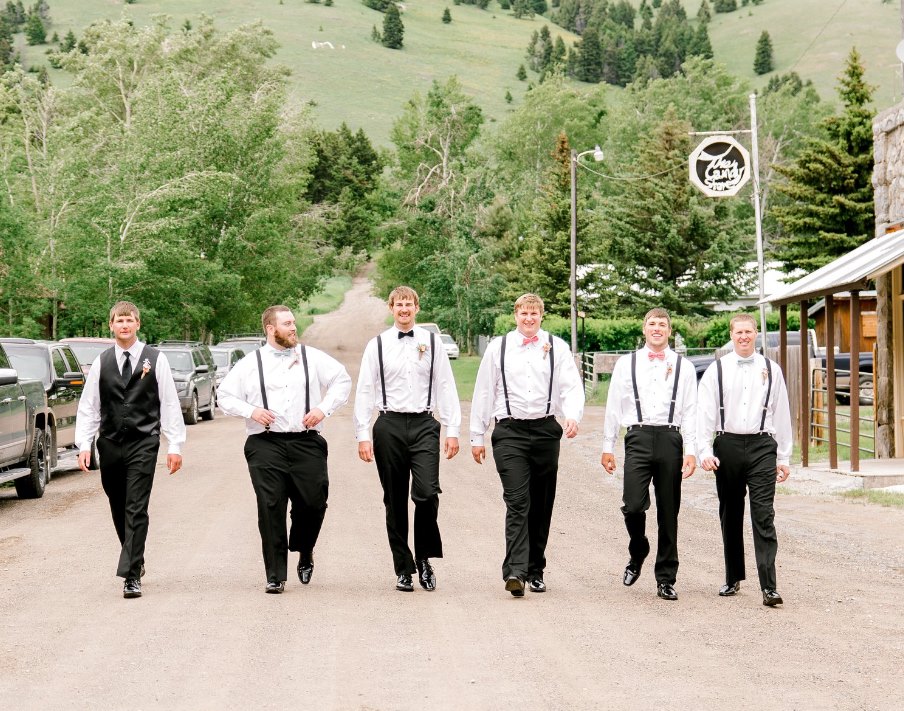 groomsmen walking down dirt road with mountains in the background