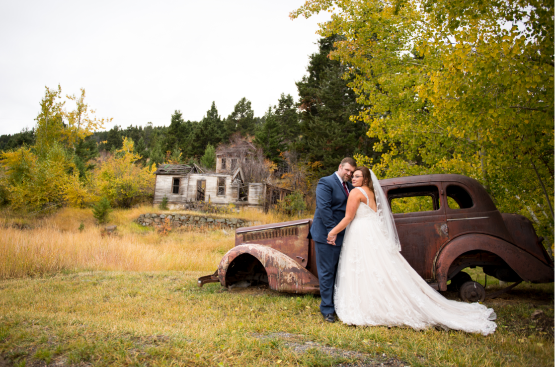 bride and groom posing next to old car and house
